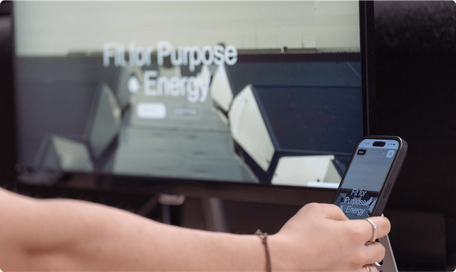 Person holding a smartphone in front of a screen displaying "Fit for Purpose Energy" with geometric shapes in the background.