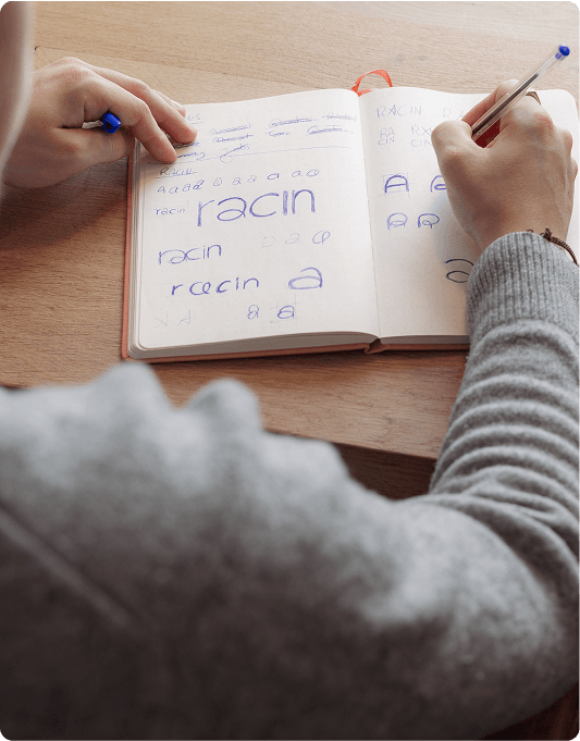 Person practicing handwriting in a notebook with various styles of the word "racin" using a blue pen.