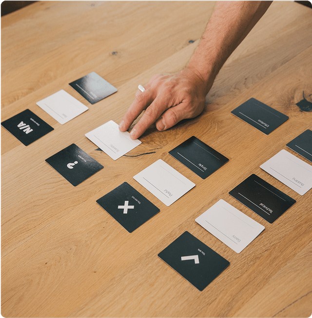 A hand arranging black and white cards with symbols and words on a wooden table.