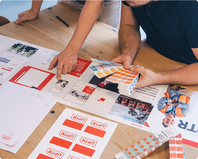 People reviewing design materials and color swatches on a wooden table, focusing on branding and layout options.