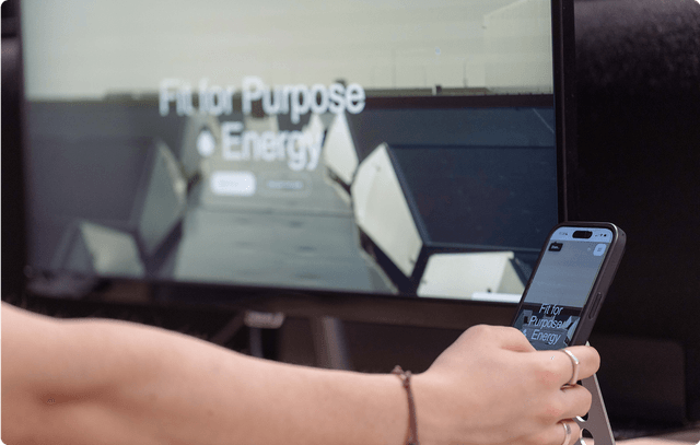 Prototype Person holding a smartphone displaying the same "Fit for Purpose Energy" webpage as the monitor in the background.