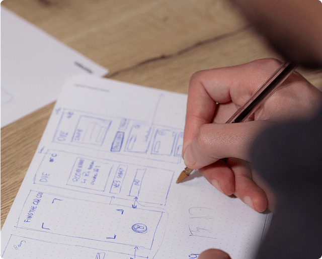 Architecture Person sketching a mobile app design on graph paper with a pencil, focusing on layout and interface elements.